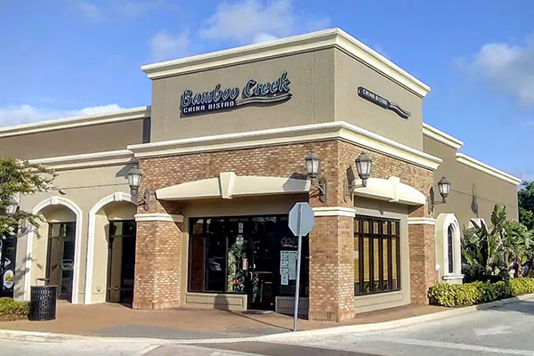 The exterior of Bamboo Creek China Bistro, a brick-and-stucco building with arched entryways, large windows, and signage above the entrance.